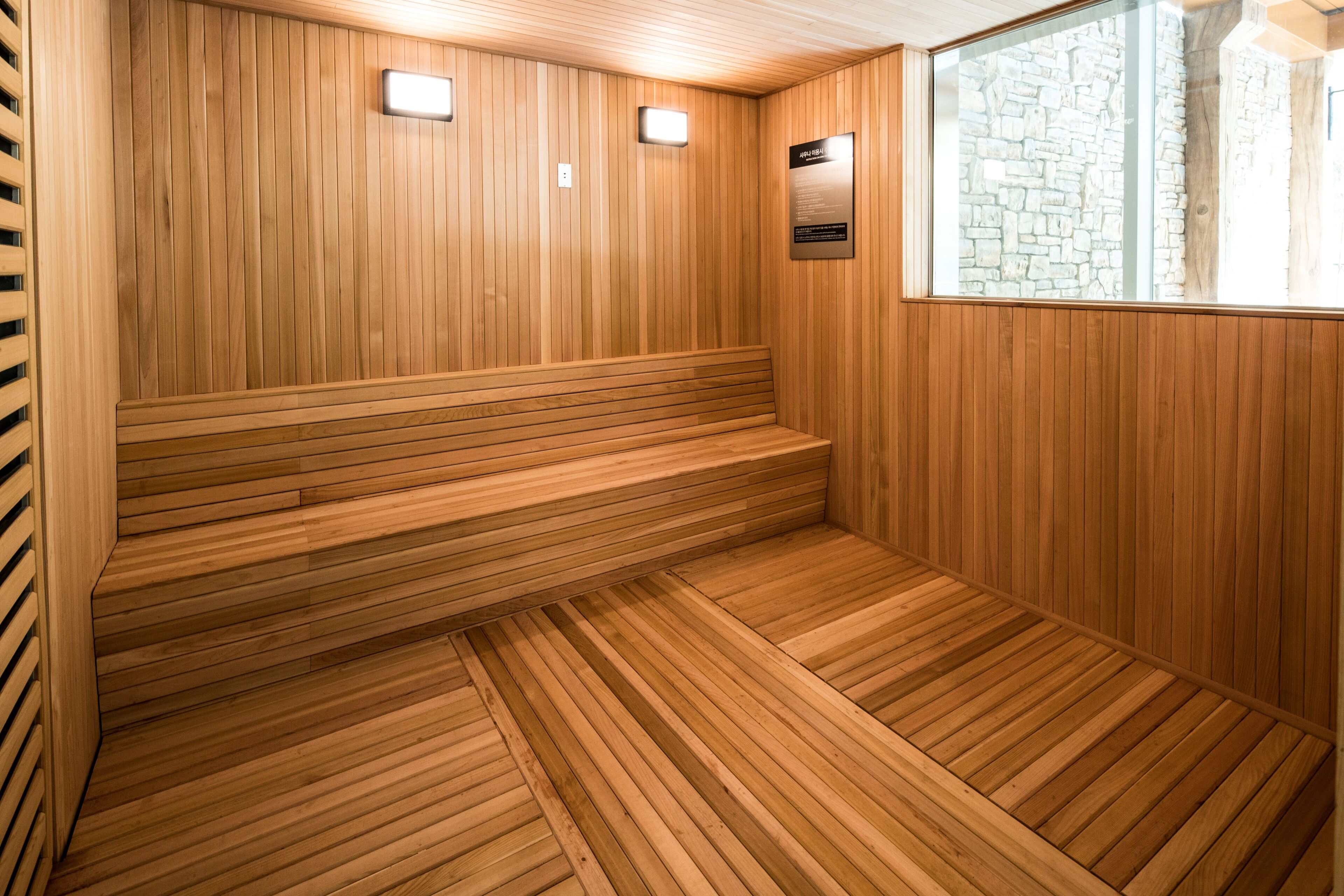 A wooden sauna with a bench, a stone wall, and a window.