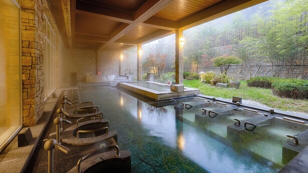 Zona de baños termales con varios tinos, paredes de piedra y vistas a un área boscosa.