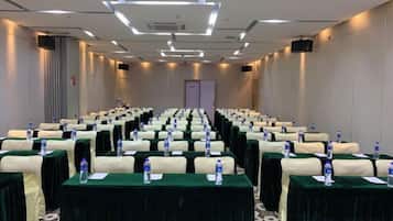 Un salón de conferencias con filas de mesas, cada una con una botella de agua y un bloc de notas.