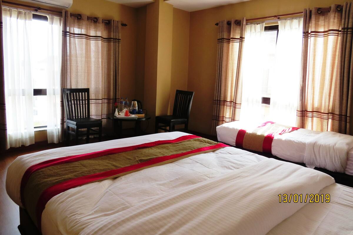 A hotel room with two beds, a table with a tray of items, and curtains on the windows.