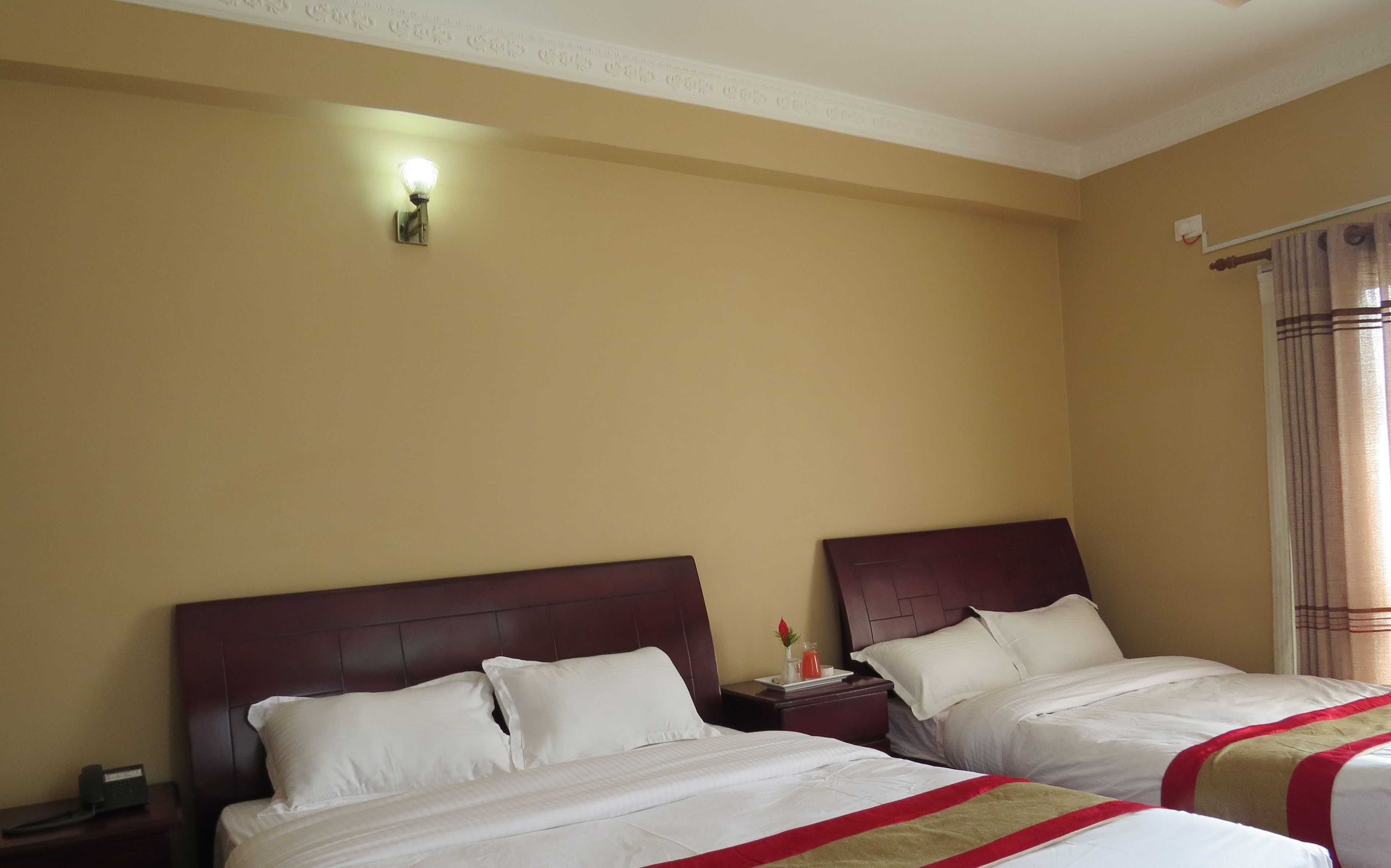 A hotel room with two beds, a nightstand with a phone, and a wall-mounted light fixture.