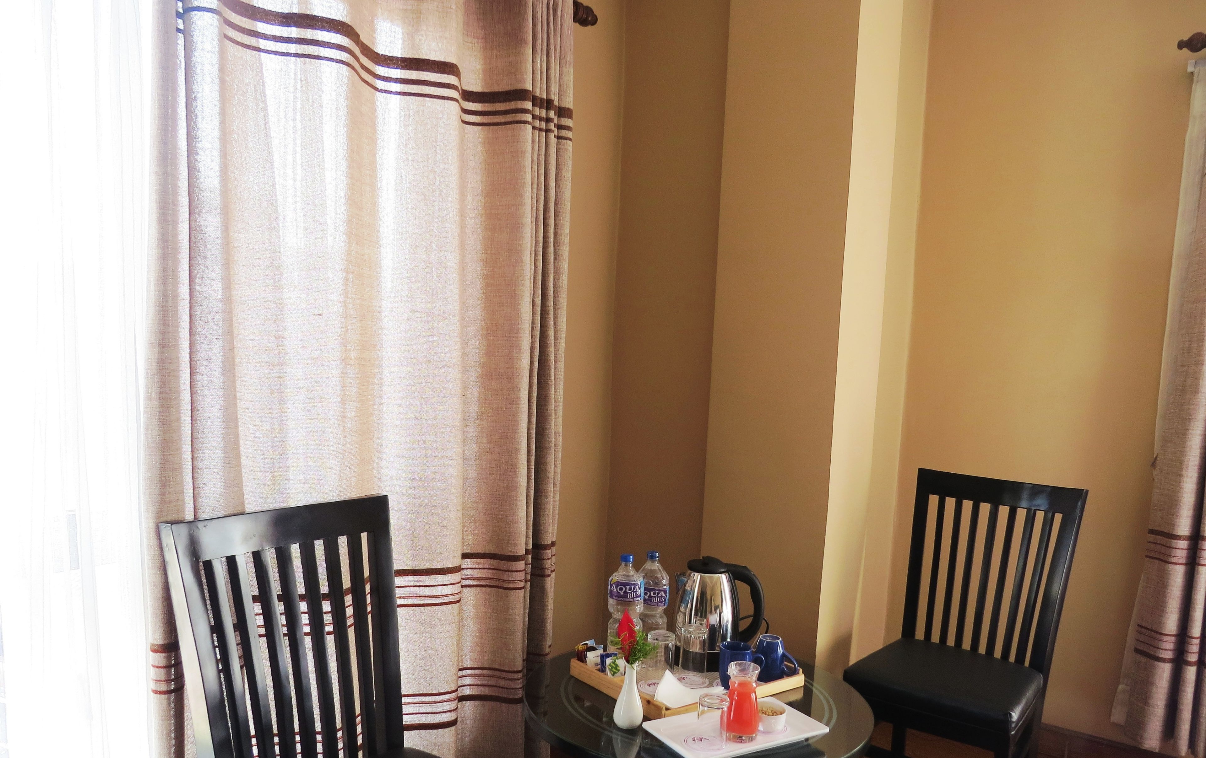 A dining area with two black chairs, a glass table, and a vase with a red flower. There are water bottles and a kettle on the table.