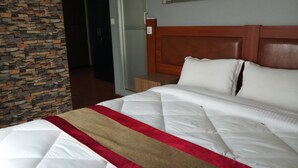 Habitación de hotel con pared de piedra, cabecera de madera y cama con ropa blanca y una manta roja y beige.