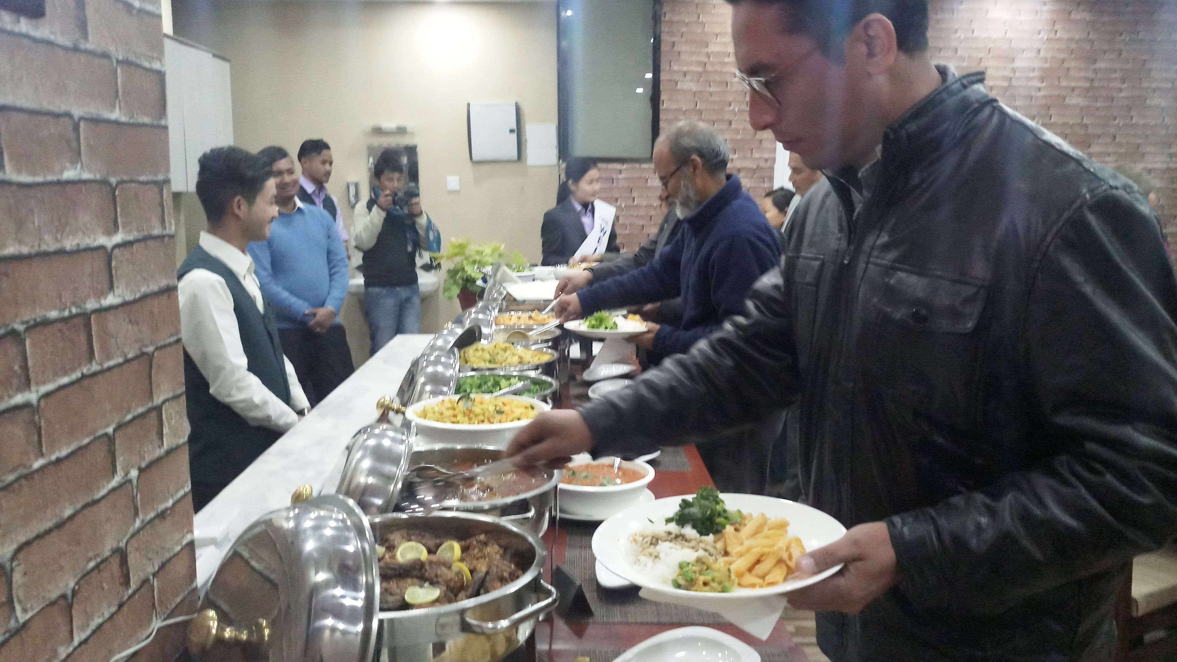 A buffet setup with various food dishes and people serving themselves.