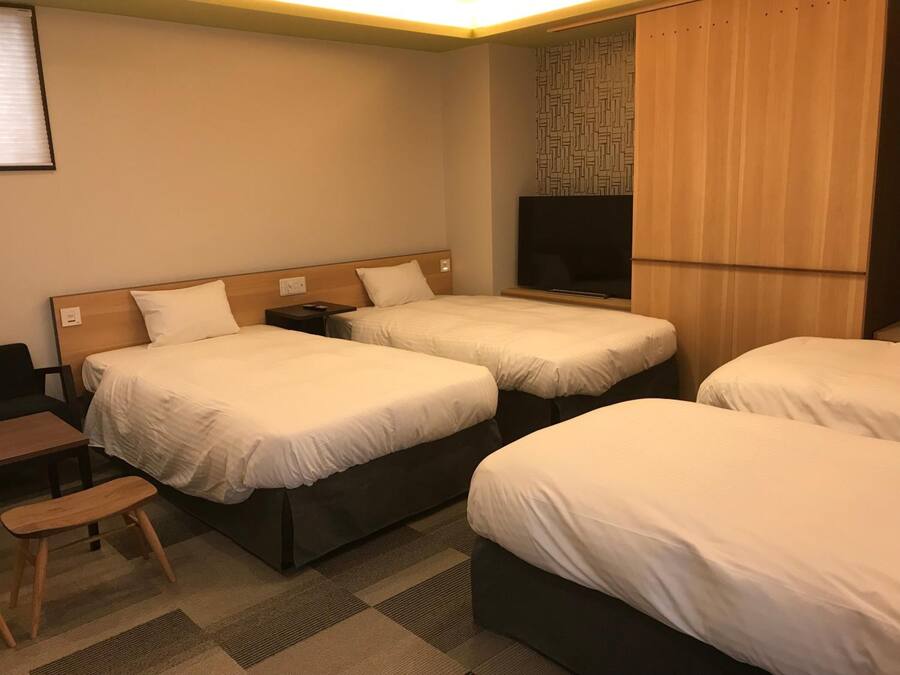 A hotel room with two beds, a desk, a chair, a TV, and a wardrobe.