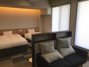 Een hotelkamer met twee bedden, een bank en een raam met zonwering.