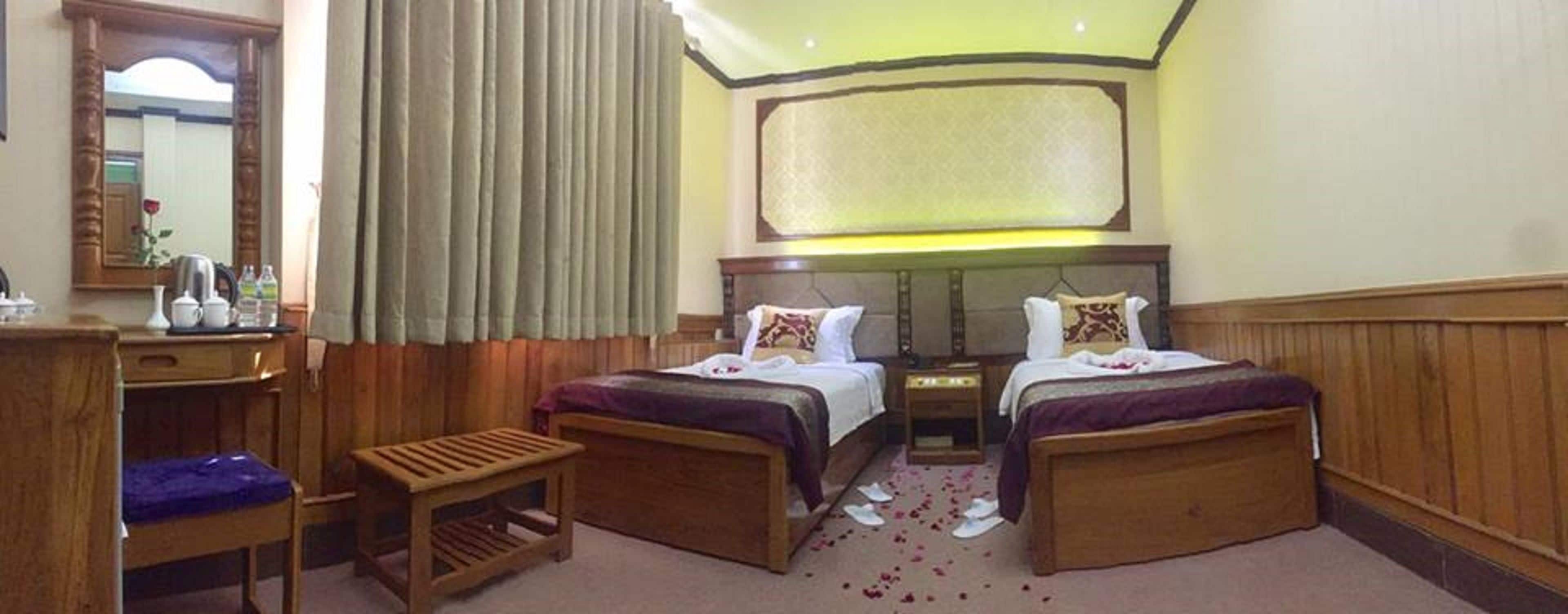 A hotel room with two wooden beds, a small wooden bench, a desk with toiletries, and a large mirror.
