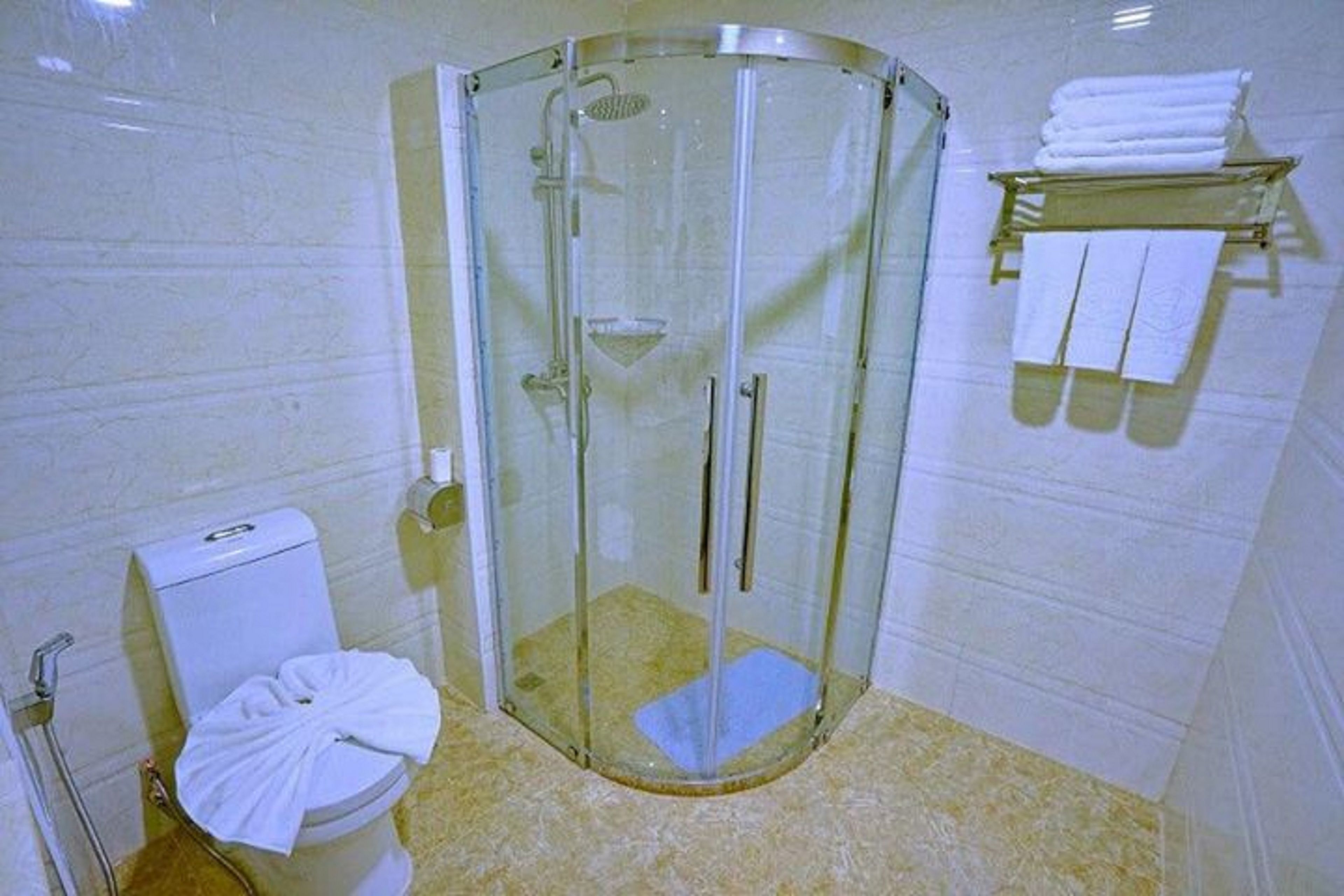 A bathroom with a glass-enclosed shower, a toilet with a towel on it, and a shelf with folded towels.