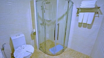 Un baño con ducha de vidrio, inodoro con una toalla encima y un estante con toallas dobladas.