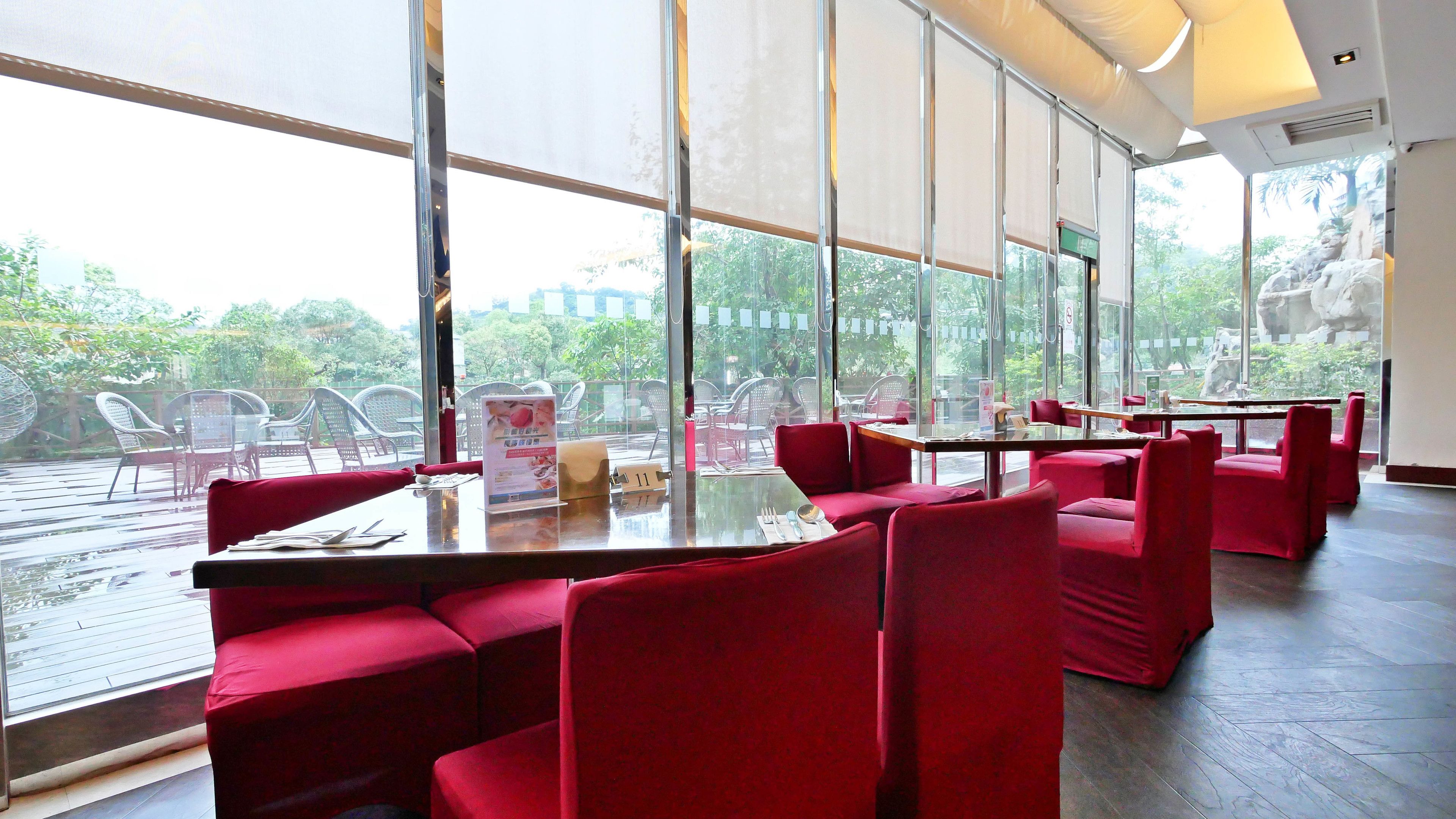 A restaurant with red seating, large windows, and a view of greenery.