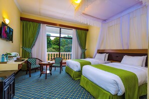 A hotel room with two beds, a desk, a chair, and a view of greenery outside.