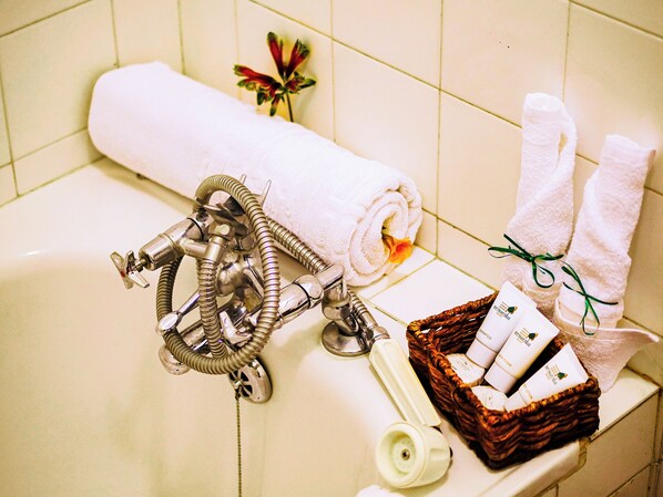 A bathroom with a bathtub, a shower head, a towel, a flower, and toiletries in a basket.