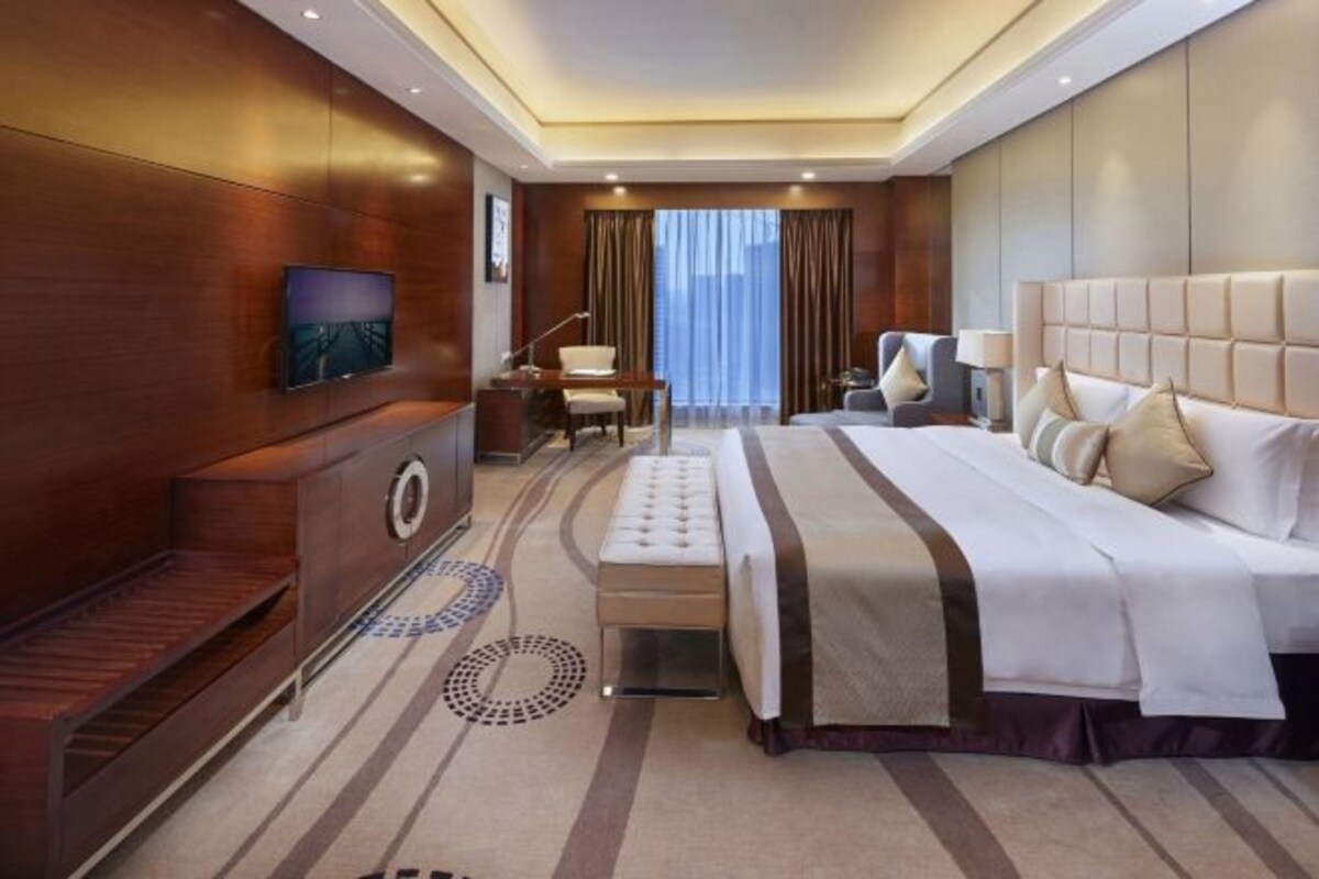 A modern hotel room with a large bed, a desk, a chair, and a television.