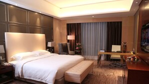 Una habitación de hotel con una cama grande, un escritorio, una silla, una lámpara y un televisor.