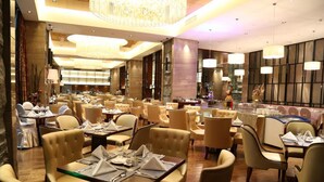 Un restaurante espacioso con varias mesas y sillas, elegantes candelabros y una decoración de interiores moderna.