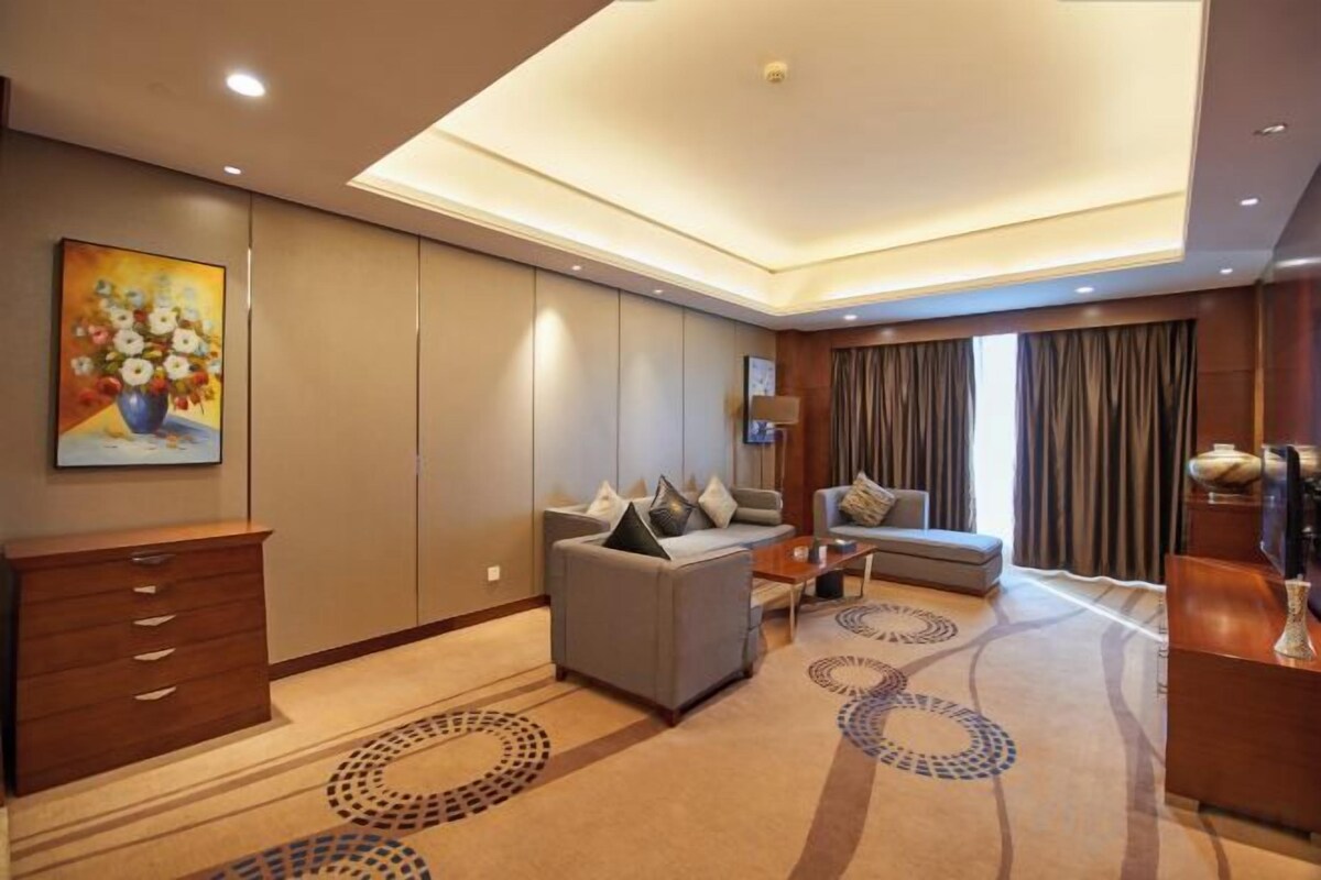 A hotel room with a sofa, a desk, a lamp, and a painting on the wall.