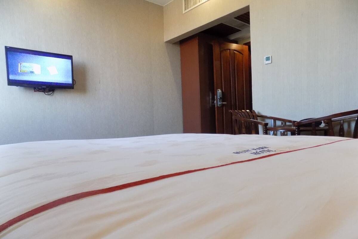 A hotel room with a bed, a television mounted on the wall, a wooden door, and a chair.