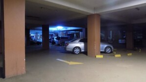 Un parking avec une voiture argentée garée près d’un pilier, des flèches jaunes indiquant la direction peintes sur le sol, et une lumière bleue en arrière-plan.