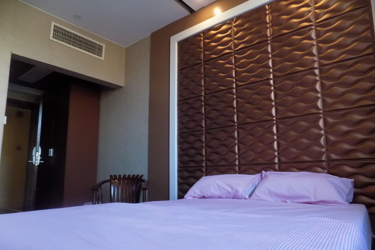 A hotel room with a large bed, a headboard with a textured pattern, a door, and a chair.