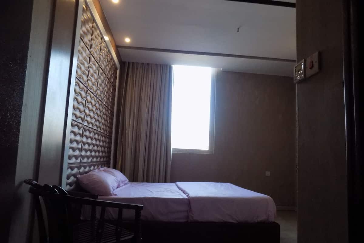 A bedroom with a bed, a chair, a window, and a wall with a textured design.
