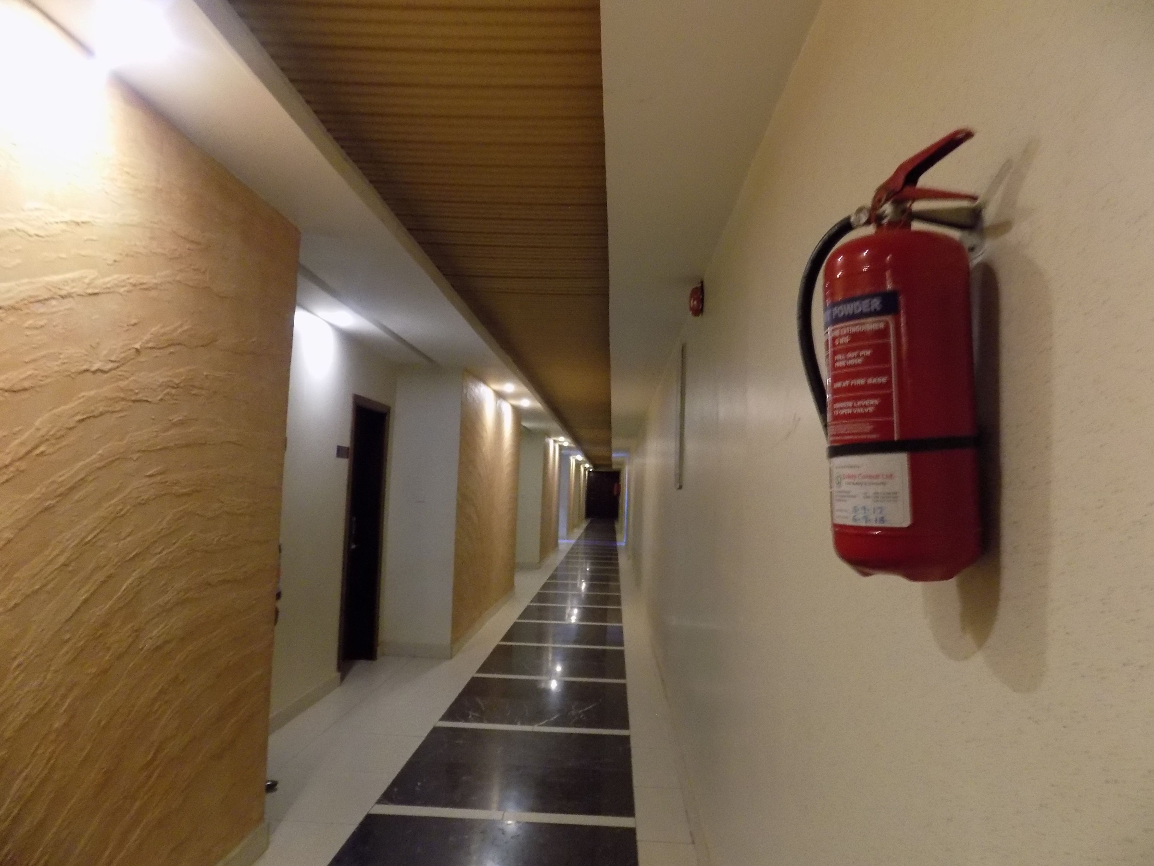 A hallway with a fire extinguisher mounted on the wall, wooden paneling on the left, and a tiled floor.