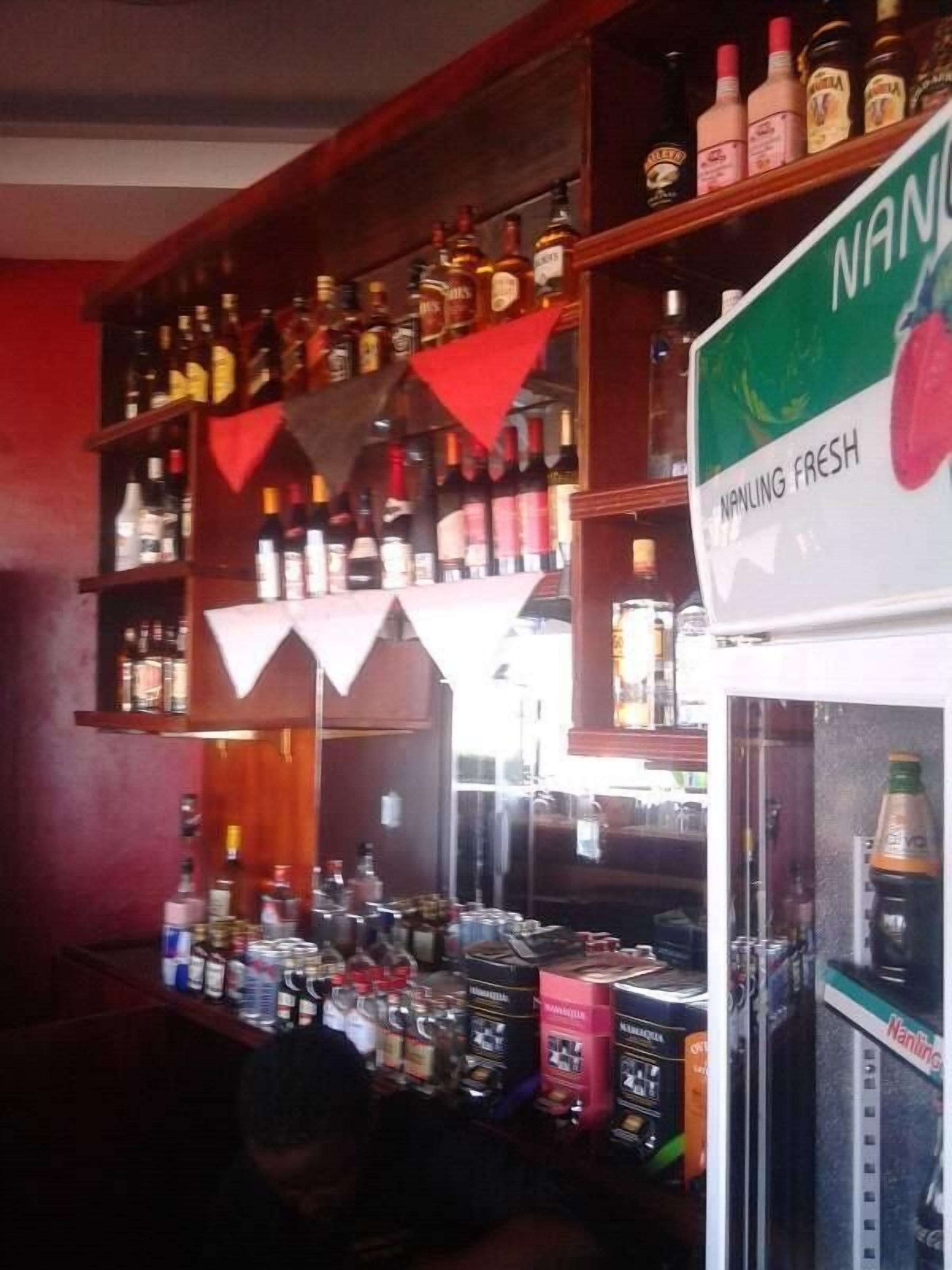 Un bar dont les étagères sont remplies de différentes bouteilles d’alcool et qui possède un présentoir réfrigéré portant l’inscription « NANLING FRAIS ».