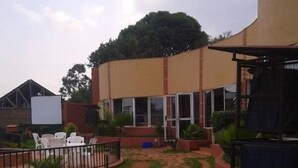 A courtyard with a stone pathway leading to a building with large windows and a covered area. - Makutano Hotel (Kampala)