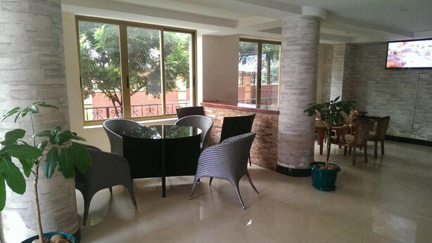 A spacious indoor area with a high ceiling, large windows, and a mix of wicker and wooden furniture. - Makutano Hotel (Kampala)