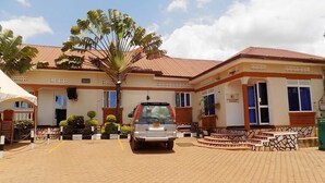 A building with a red roof, a paved entrance, and a parked car. - Star Royal Motel (Kampala)