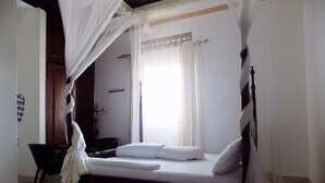 A bedroom with a canopy bed, a bedside table, and a window with curtains. - Star Royal Motel (Kampala)