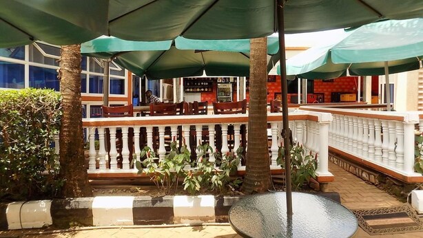 An outdoor seating area with green umbrellas, a glass table, and a view of the restaurant in the background. - Star Royal Motel (Kampala)