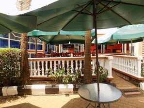 Un espace extérieur aménagé avec des parasols verts, une table en verre et une vue sur le restaurant en arrière-plan.