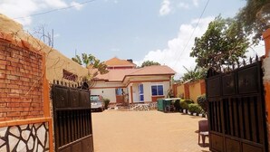A gated residential area with a paved driveway leading to a house with a tiled roof. - Star Royal Motel (Kampala)