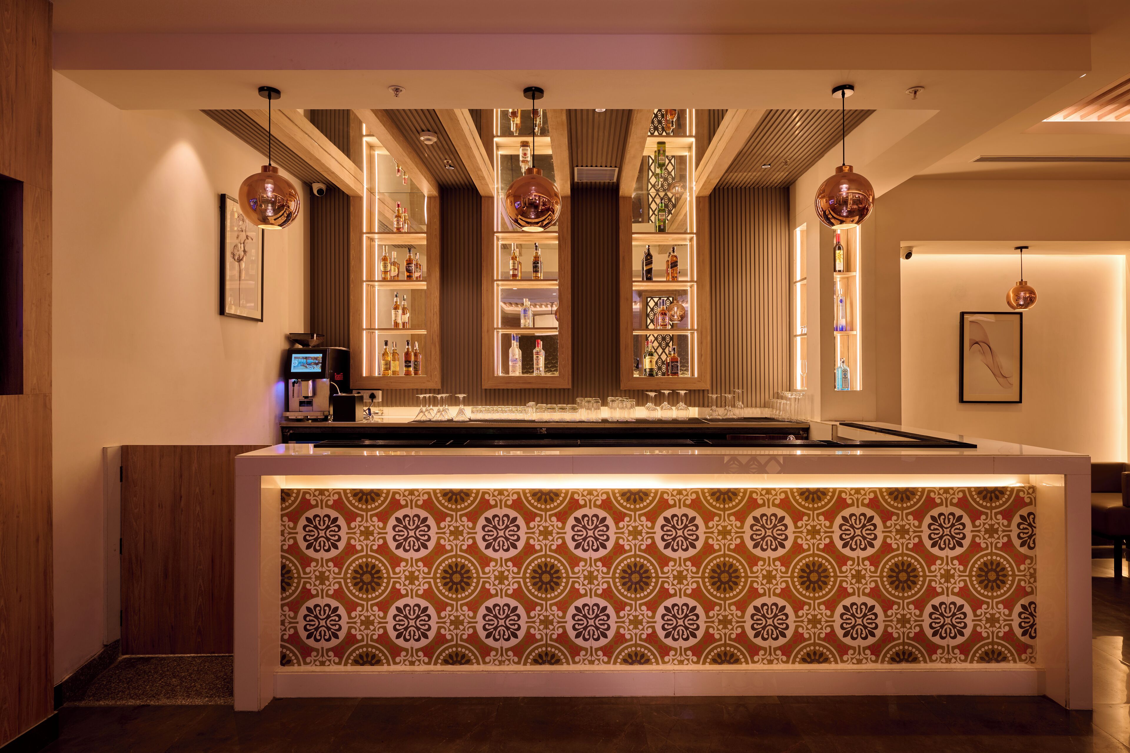 A bar area with patterned wallpaper, shelves of bottles, and pendant lighting.