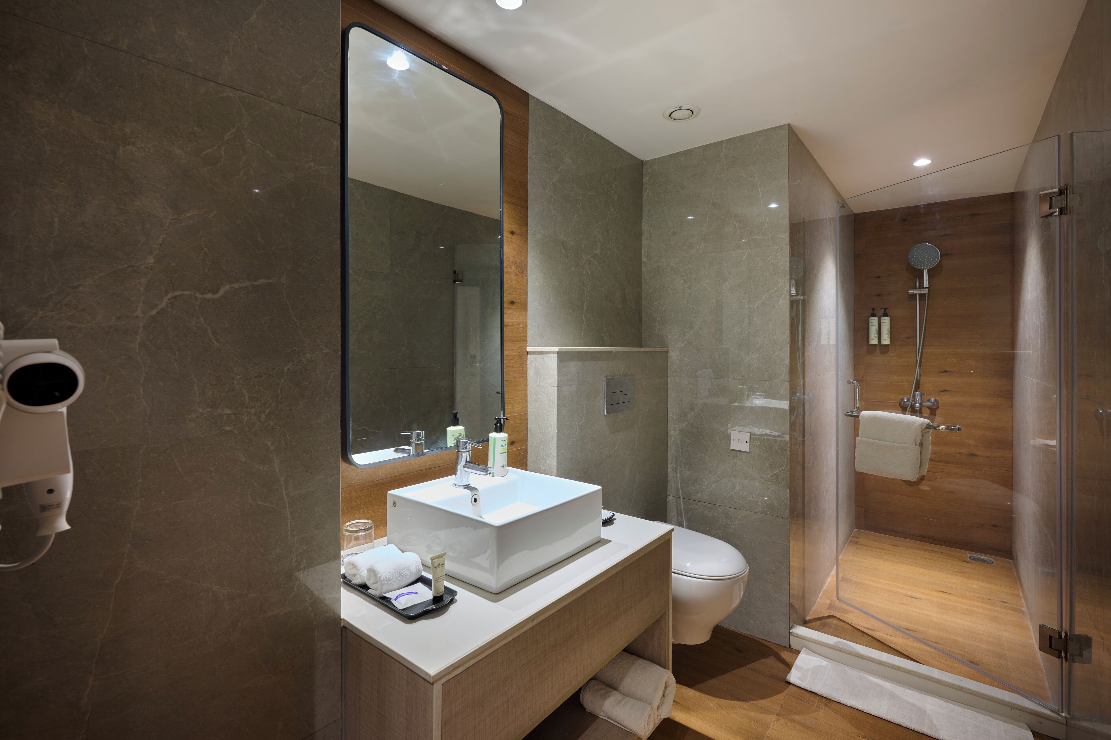 A modern bathroom with a large mirror, a white sink, a toilet, and a glass-enclosed shower area.