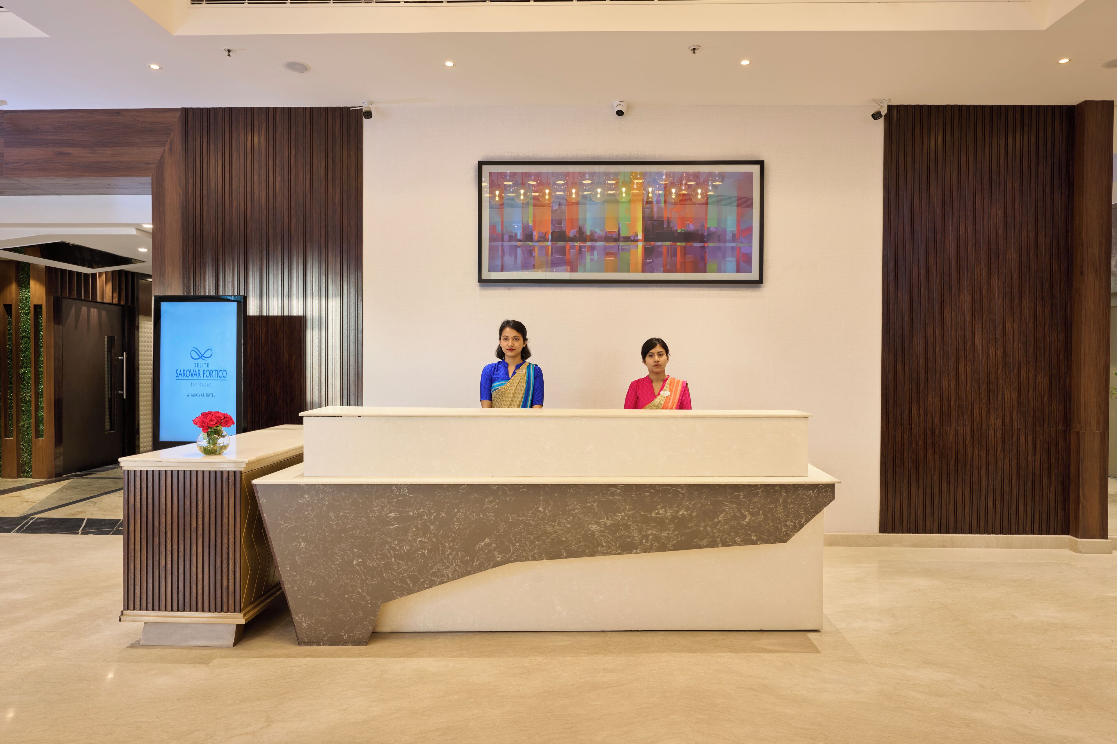 A reception desk with two staff members, a digital screen, and a colorful abstract painting on the wall.