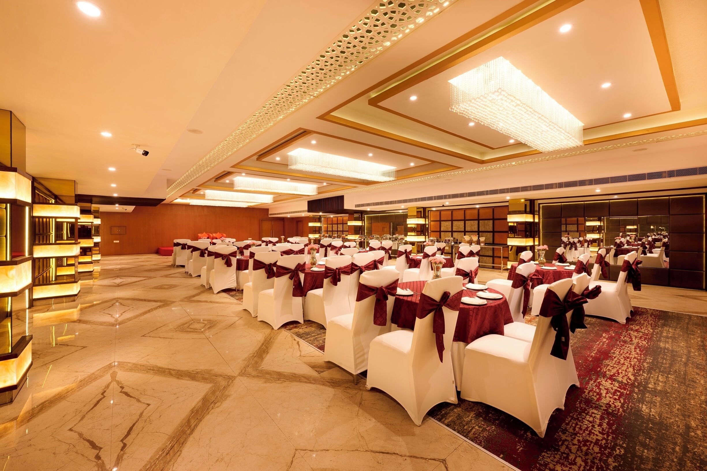 A banquet hall with rows of white chairs with red sashes, tables with red tablecloths, and a chandelier.