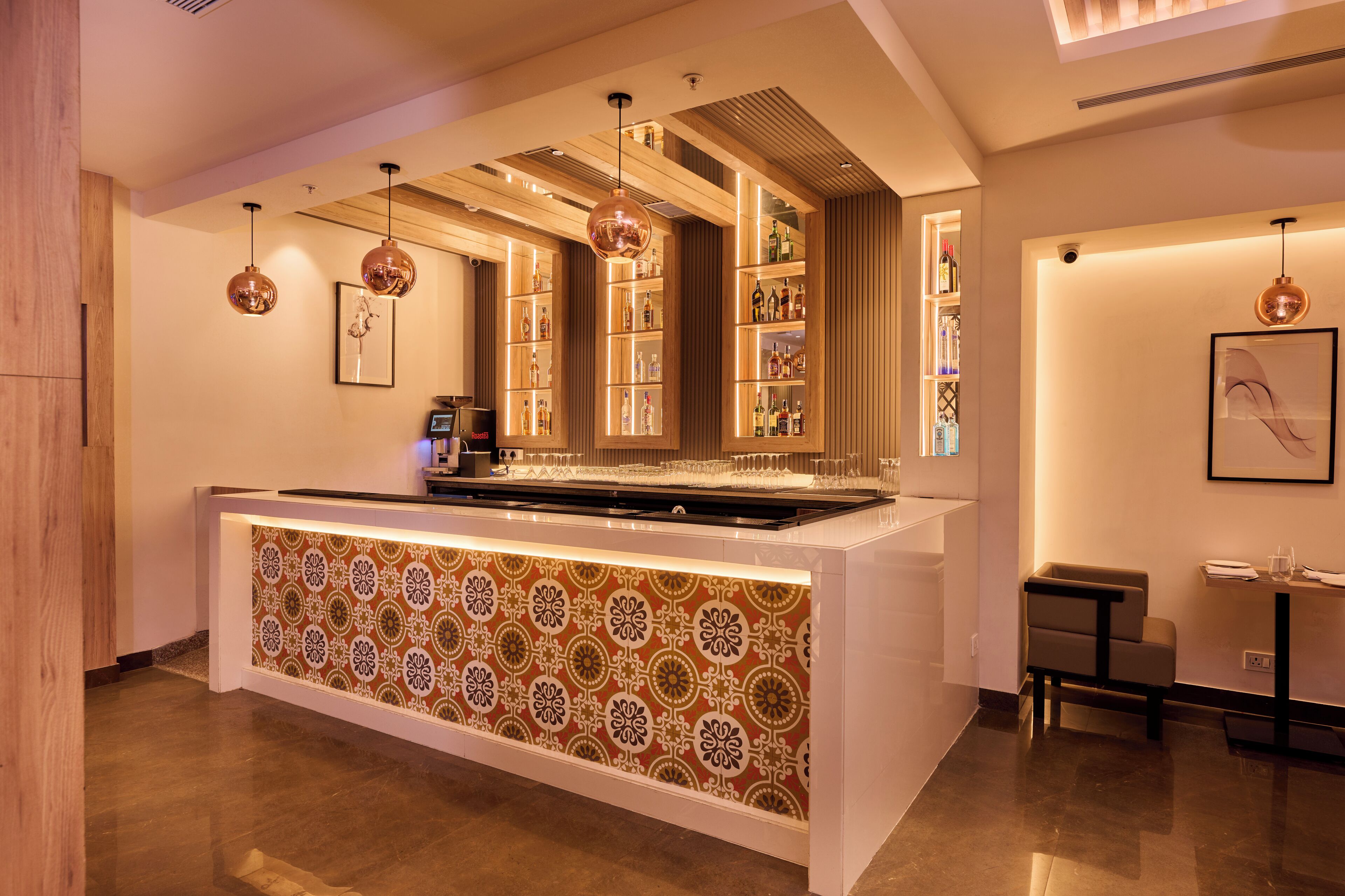 A modern bar area with a patterned counter, hanging pendant lights, and shelves stocked with bottles.