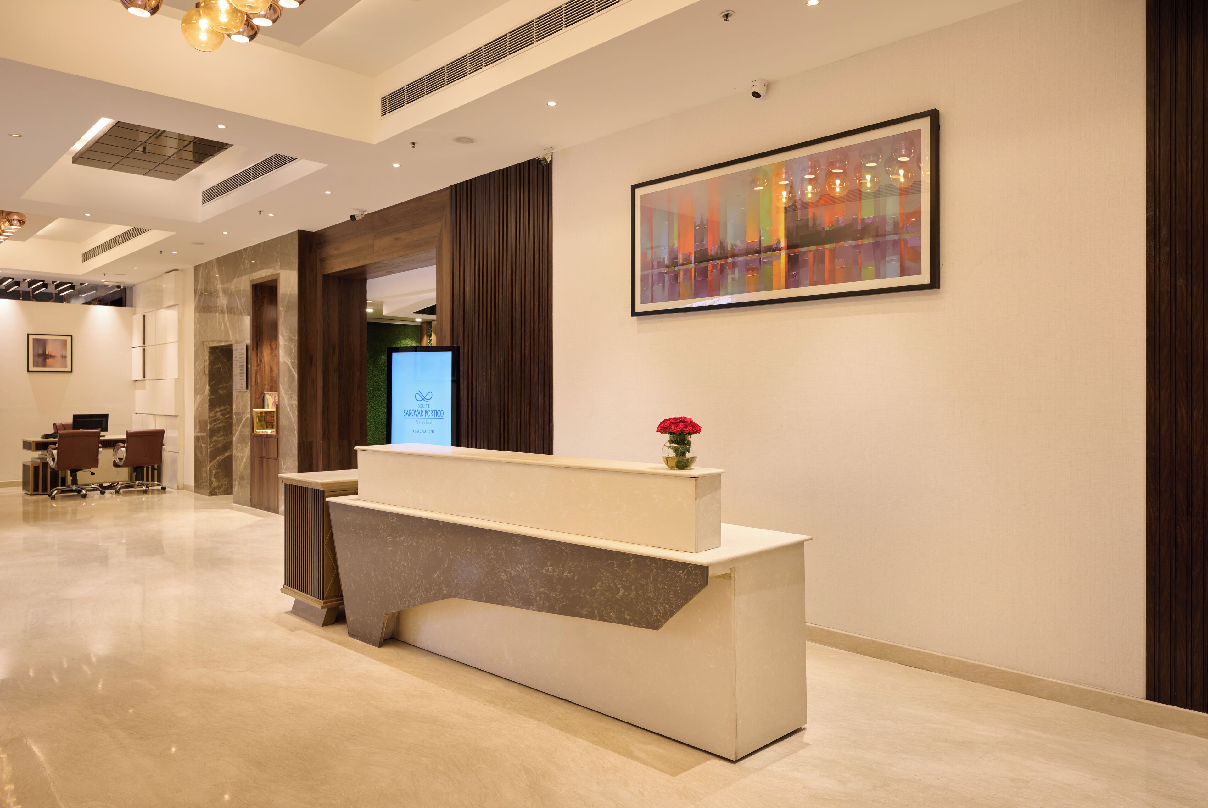 A modern reception area with a marble reception desk, a digital screen, and a framed abstract painting.