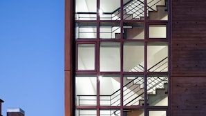Ein modernes Gebäude mit Glasfassade und sichtbarer Treppe, ein klarer Himmel darüber.