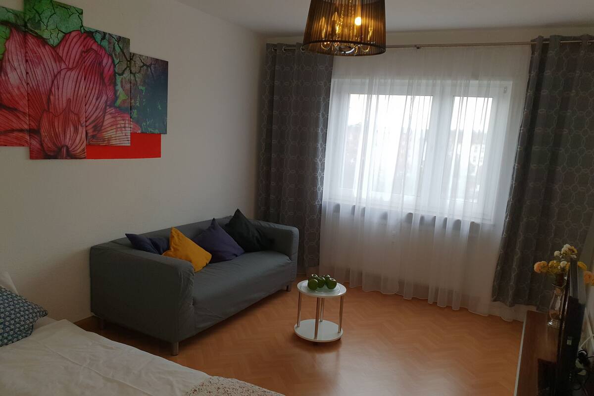 Una sala de estar con un sofá gris, una mesita redonda y una cama.