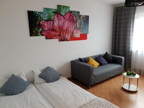 Una habitación con una cama, un sofá gris y una pequeña mesa con manzanas.