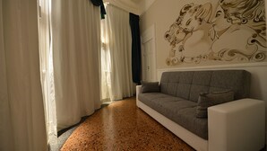 A living room with a grey sofa, a wall mural, and a window with curtains. - Conte di cavour (Foggia)