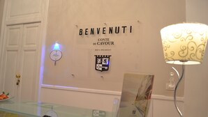 A reception area with a 'BENVENUTI' sign, a coat of arms, and a lamp. - Conte di cavour (Foggia)