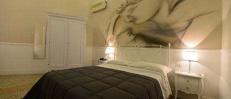 Un dormitorio con cama, mesita de noche, espejo y un mural en la pared.