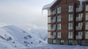 A multi-story building with a wooden facade and multiple balconies, surrounded by snow-covered mountains. - Powderinn (Kazbegi)
