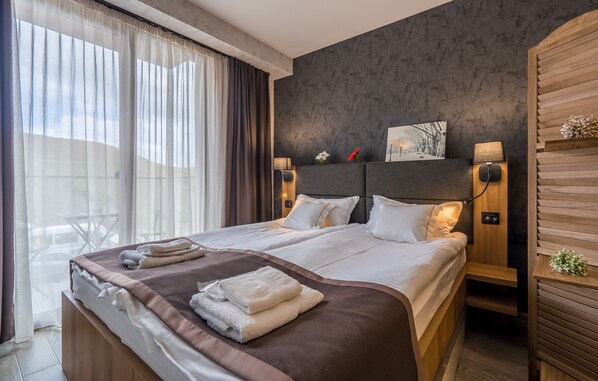 A modern hotel room with a large bed, two bedside tables, a nightstand, a window with curtains, and a view of the outdoors. - Powderinn (Kazbegi)