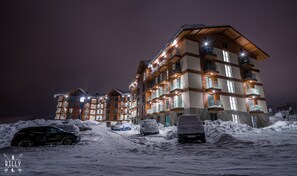 A multi-story hotel with balconies and illuminated windows at night. - Powderinn (Kazbegi)