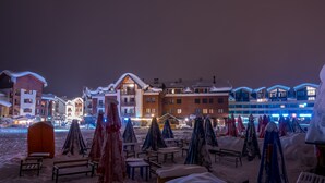 A snow-covered outdoor area with multiple buildings, including a prominent hotel with a lit-up facade.
