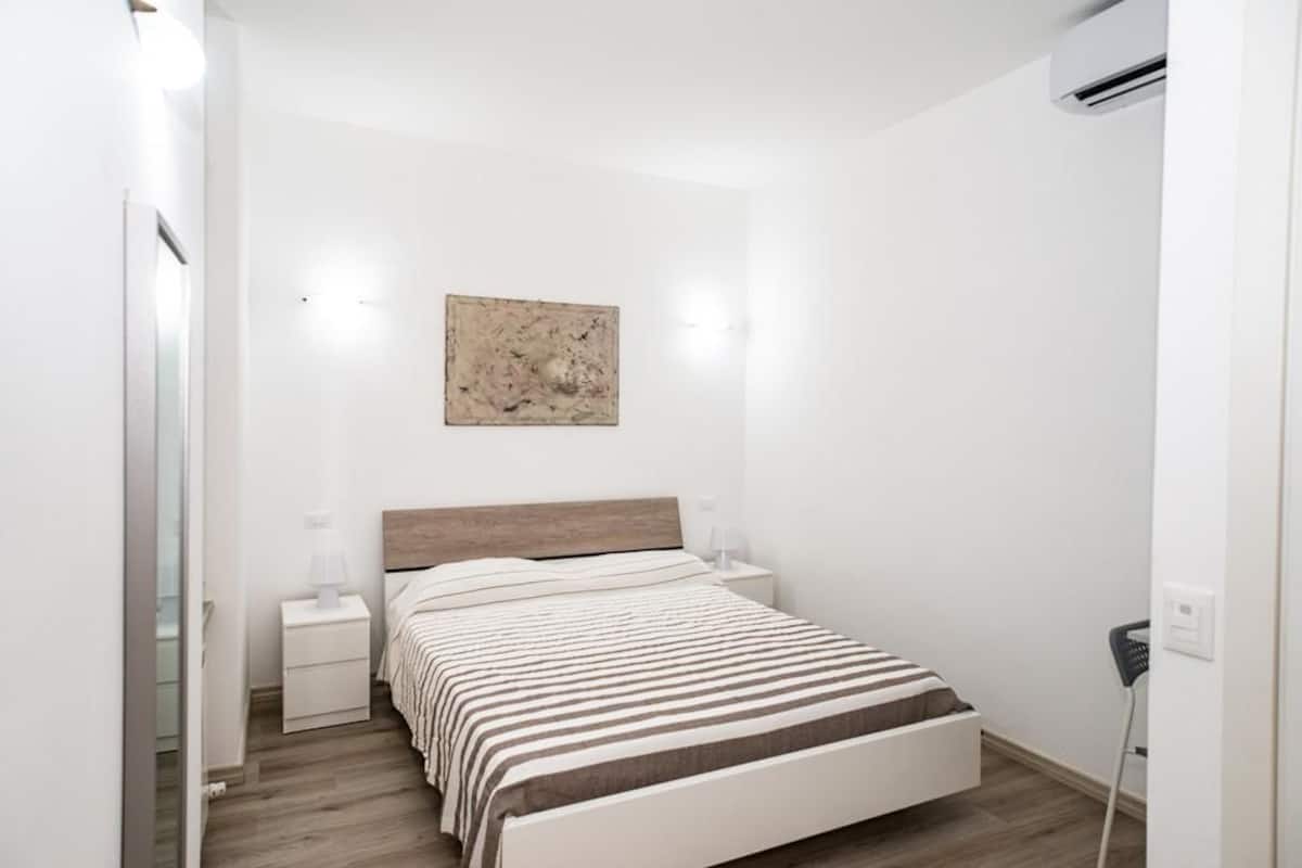 A minimalist bedroom with a bed, bedside tables, and a wall-mounted artwork.